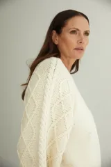 Buzo de lana fina sin teñir con cuello redondo y mangas raglán. Presenta un diseño de tejido de punto con dibujo de cables en las mangas y cuerpo liso.