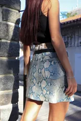 Minifalda con estampado de piel de serpiente en tonos celeste y blanco, con pretina ancha color crudo y cinturón fino negro.