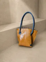 Cartera de cuero con textura crocco en color rojo, de silueta estructurada, manijas largas marrones y detalles de terminación artesanal en el borde superior.