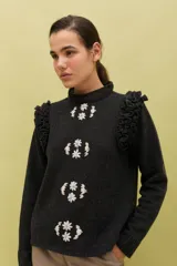 Sweater de lana color celeste, con cuello redondo, mangas largas y volados decorativos en los hombros. Presenta bordados florales artesanales en el frente y detalles de tejido calado vertical.