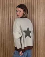 Buzo de punto de algodón color crudo, con diseño holgado y mangas largas. Presenta detalles en marrón en el cuello, puños y ruedo, y un gran diseño de estrella verde militar en la espalda.