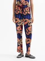 Babucha de algodón con estampado floral y de serpientes en tonos naranja, azul y verde sobre fondo azul marino. Tiene cintura elastizada con cordón ajustable y calce regular.