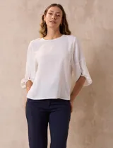 Blusa de gasa con estampado geométrico en tonos negro, gris y celeste. Tiene cuello redondo y mangas 3/4 amplias con abertura y botón.