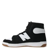 Championes de caña media New Balance modelo 480, con diseño inspirado en el básquetbol. Presentan una combinación de colores negro y blanco, con el logo 'N' característico en los laterales, puntera perforada y suela de goma color caramelo.