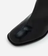Bota de caña baja en cuero sintético color negro, con punta cuadrada y taco bloque de altura media con textura amaderada.