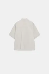 Camisa de corte fluido con cuello solapa y manga corta con dobladillo. Presenta cierre frontal con botones ocultos bajo una tapeta.