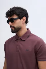 Remera polo bordó con textura sutil, cuello y puños acanalados con línea oscura de contraste, cierre frontal parcial de dos botones y logo bordado en el pecho.