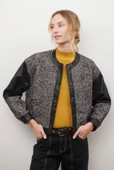 Chaqueta bomber color bordó con mangas de cuero sintético marrón y cuerpo de tweed con patrón de espiga. Cierre frontal con botones a presión y cuello redondo.