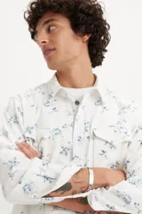 Camisa de hombre de corte relajado, color blanco con estampado floral azul, con cuello clásico, cierre con botones a presión, mangas largas con puños abotonados y dos bolsillos con solapa abotonada en el pecho.