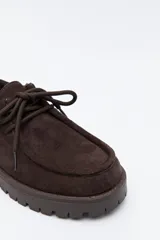 Zapato de gamuza color marrón con cordones, puntera con costura marcada y suela robusta dentada.