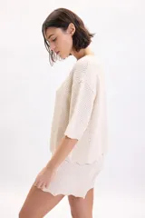 Sweater color crudo de manga corta, confeccionado en tejido de punto con diseño de textura fantasía, cuello redondo y corte holgado.