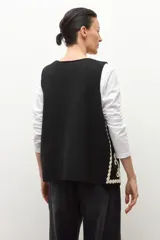 Chaleco tejido negro con escote en V, sin mangas y bordados en color crema con motivos florales y detalles de ondas en los bordes.