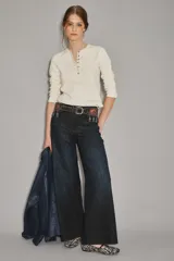 Jean de corte oxford y tiro alto, confeccionado en denim azul oscuro con un ligero lavado. Presenta un diseño de pierna ancha que se ensancha desde la cadera hacia el ruedo, con cierre y botón frontal.