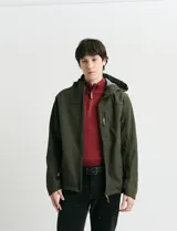 Campera softshell color verde militar, con capucha ajustable, cierre frontal completo y bolsillo vertical en el pecho con detalles en naranja.