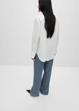Camisa de corte oversize confeccionada en tejido popelín de mezcla de algodón y lyocell. Presenta diseño recto, cuello camisero, cierre frontal con botones y manga larga con puños abotonados. Incluye un sutil detalle bordado en el pecho.
