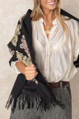 Pashmina de tela densa y suave, con caída pesada y diseño bordado con motivos florales en tonos dorados y beige. Presenta terminaciones con flecos en los extremos.