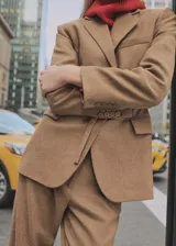 Blazer de corte recto en color tostado, confeccionado en tejido mezcla de lana virgen. Presenta cuello con solapas de muesca, cierre frontal, bolsillos laterales con solapa y detalle de cinturón integrado con hebilla en la cintura. Las mangas largas cuentan con puños abotonados.