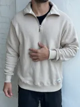 Buzo beige de felpa con cuello alto y cierre metálico a la mitad del torso.