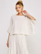 Blusa corta color beige de lino y viscosa, con escote redondo, mangas tres cuartos estilo kimono y corte holgado.