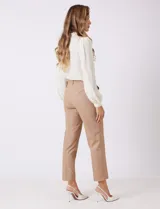 Pantalon de corte cigarette en color beige, confeccionado en tejido con apariencia denim y acabado satinado. Presenta tiro medio-alto, largo tobillero, cintura con presillas, cierre con gancho sastrero oculto, bolsillos laterales diagonales con botones forrados y pinzas traseras para un ajuste entallado.