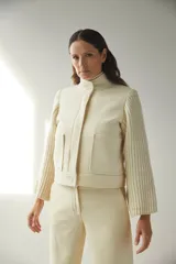 Campera de lana fina color crema, con cuerpo estructurado y mangas de tejido de punto acanalado. Presenta cuello alto, cierre frontal con botones y bolsillos laterales con doble abertura.
