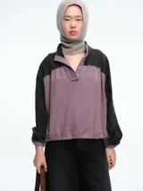 Campera de estilo casual con diseño bicolor, combinando paneles en color gris oscuro y malva. Presenta cuello alto con cierre frontal de botones a presión, mangas largas con puños elásticos y ruedo ajustable con cordón.