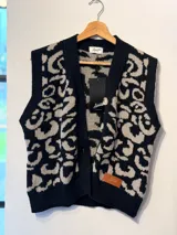 Chaleco tejido con diseño de animal print en tonos gris y negro, con borde frontal y tapeta de botones en color rojo vibrante.