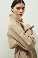 Gabardina midi de doble botonadura con diseño oversized, solapas de muesca, cierre frontal con botones y cinturón extraíble para atar en la cintura. Presenta mangas raglán con trabillas ajustables en los puños, bolsillos laterales y abertura posterior.