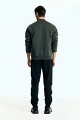 Campera bomber deportiva de tejido funcional color verde oscuro, con cuello elevado corto, cierre bidireccional y mangas raglán. Posee bolsillos delanteros con cierre y costuras selladas.