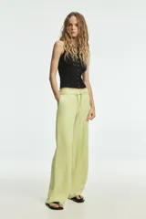 Pantalón de tiro medio confeccionado en mezcla de lino, con cintura ajustable mediante lazada, trabillas, bolsillos laterales y cierre frontal con cremallera y botón.