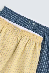 Pack de dos calzoncillos tipo bóxer de popelín de algodón. Uno es amarillo con rayas verticales azules y el otro es azul oscuro con estampado a cuadros. Ambos tienen cintura elástica con efecto doble combinado a contraste y bragueta delantera con botones.