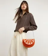 Cartera tipo hobo con diseño creativo en forma de rodaja de naranja, confeccionada con abalorios texturizados en tonos naranja y blanco. Cuenta con una correa de cadena metálica fina para llevar de forma transversal y cierre de tapa.