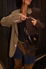 Bandolera de cuero color beige con correa ajustable y logo metálico dorado en el frente.