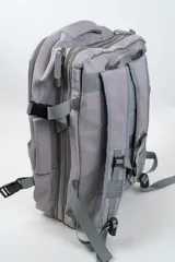 Mochila de viaje color gris, con diseño funcional que incluye múltiples compartimentos con cierre, bolsillo frontal vertical y correas ajustables con hebillas.