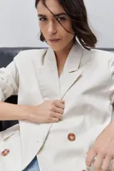 Blazer de silueta amplia y largo por debajo de la cadera, color marfil, confeccionado en tela suave y liviana. Presenta cuello con solapas, hombreras, manga larga y cierre cruzado con botones carey.