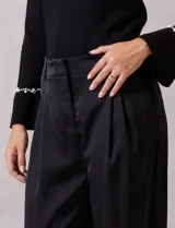 Pantalón palazzo de satén color negro, de tiro alto con pretina delantera estructurada, pasadores para cinturón y bolsillos laterales. Presenta una caída fluida y amplia, con elástico en la parte posterior de la cintura para mayor ajuste.
