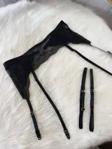 Portaligas de encaje negro con tiras elásticas ajustables y broches metálicos para sujetar medias.