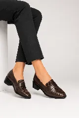 Mocasín clásico de cuero negro, con taco bajo y ancho de 4 cm. Combina laterales lisos con un panel frontal de acabado brillante y textura sutil, con una banda ancha sobre el empeine.