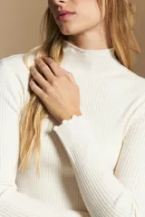 Polera de tejido acanalado con cuello alto, corte ajustado al cuerpo y mangas tres cuartos con terminaciones onduladas en los puños.