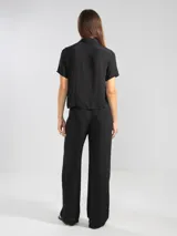 Pantalón palazzo negro de crepe con cintura elastizada, bolsillos laterales y terminaciones en cobre.