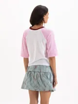 Remera estilo raglán de manga corta, con cuerpo blanco, mangas rosadas y cuello redondo bordó. Cuenta con un estampado frontal en azul con las palabras 'IBIZA 84' y detalles de encaje en las costuras de las sisas.