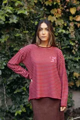 Remerón de manga larga con diseño de rayas horizontales finas en tonos tierra. Presenta un corte holgado y cuenta con un bordado artesanal en color rojo en el pecho.
