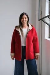 Tapado de paño rojo con capucha, cierre frontal y detalles en color beige en el interior, puños y bordes de los bolsillos. Presenta un corte recto y holgado.