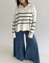 Sweater de tejido bremer con diseño a rayas horizontales negras sobre fondo blanco, corte amplio, cuello tipo polo con cierre frontal y mangas largas con puños acanalados.