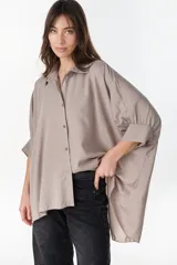 Camisa oversize de color beige, con mangas murciélago amplias, puños fruncidos con elástico y cierre frontal de botones.