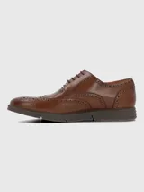 Zapato tipo oxford de cuero color marrón con diseño brogue, cordones al tono y suela de goma tipo deportiva.