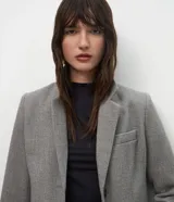 Abrigo largo de corte slim, color gris con textura jaspeada. Presenta solapas clásicas, cierre frontal con botones, bolsillos laterales con solapa y abertura trasera. Incluye forro interno.