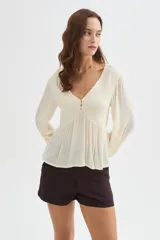 Blusa blanca de viscosa, con cuello en V, detalles de frunces en el frente, botones decorativos y mangas largas holgadas.