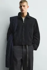 Cazadora de corte regular fit confeccionada en tejido jacquard con textura abstracta. Presenta cuello solapa, cierre frontal de cremallera, bolsillos de vivo en la cadera y mangas largas con puños ajustables mediante botón a presión oculto.