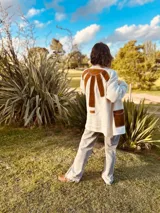 Tapado tejido en lana color crema con apliques de cuero marrón en la espalda y bolsillos delanteros. Presenta un diseño de corte largo y holgado con costuras visibles que unen los materiales.